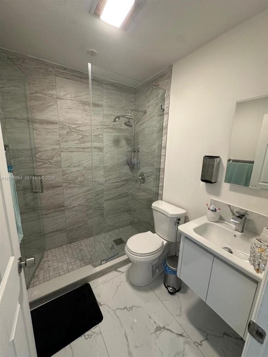Walk-in shower with floor-to-ceiling tile, glass enclosure, and rainfall showerhead, accompanied by a wall-mounted vanity with integrated sink and large-format tile flooring