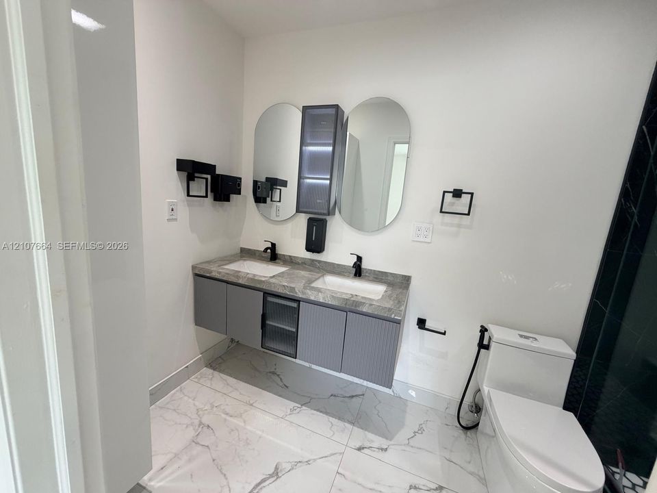 Floating double vanity featuring grey textured cabinetry, a stone-patterned countertop, dual rectangular undermount sinks, and matte black hardware paired with two oval-shaped mirrors