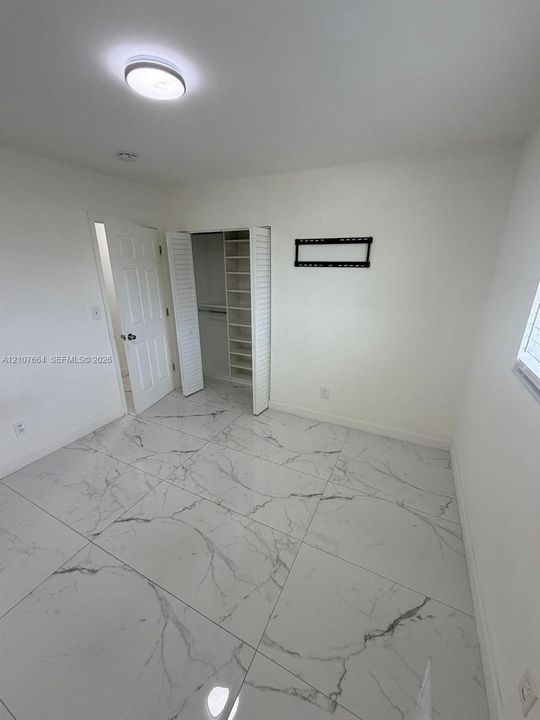 Large-format stone-finish floor tiling, built-in closet shelving, bifold closet doors, six-panel interior door, and flush-mount ceiling lighting