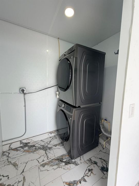 Utility space featuring large-format marble-patterned porcelain floor tile, recessed ceiling lighting, and stackable laundry appliances