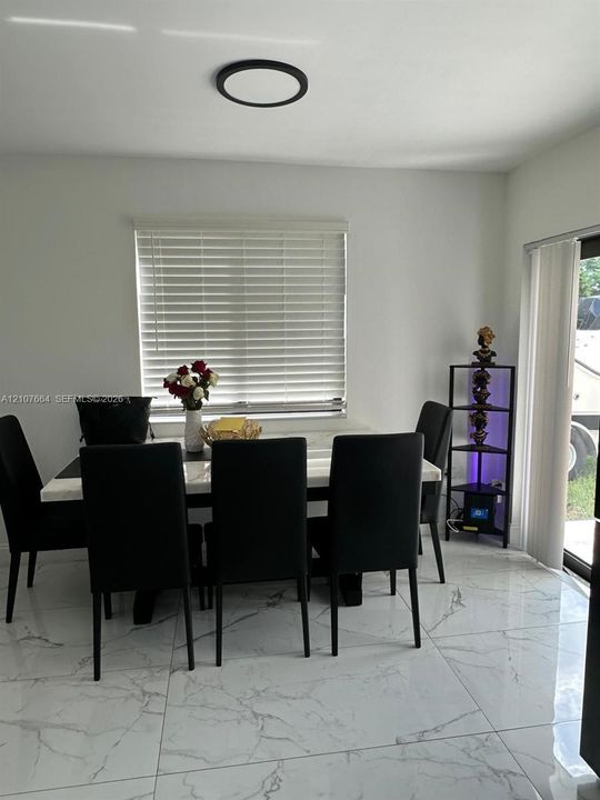 Large-format stone-finish tile flooring, recessed circular ceiling lighting, and vertical window blinds