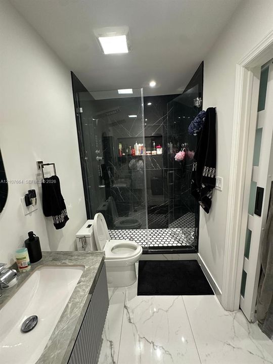 Bathroom featuring large-format white tile flooring with grey veining, a floating vanity with a stone-top integrated sink, a glass-enclosed shower with black tile surround, a built-in shower niche, and a sliding door