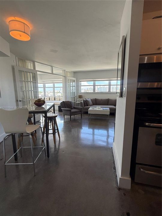 Open-concept floor plan featuring polished concrete flooring, multi-pane French doors, expansive windows with exterior scenery, and integrated stainless steel kitchen appliances