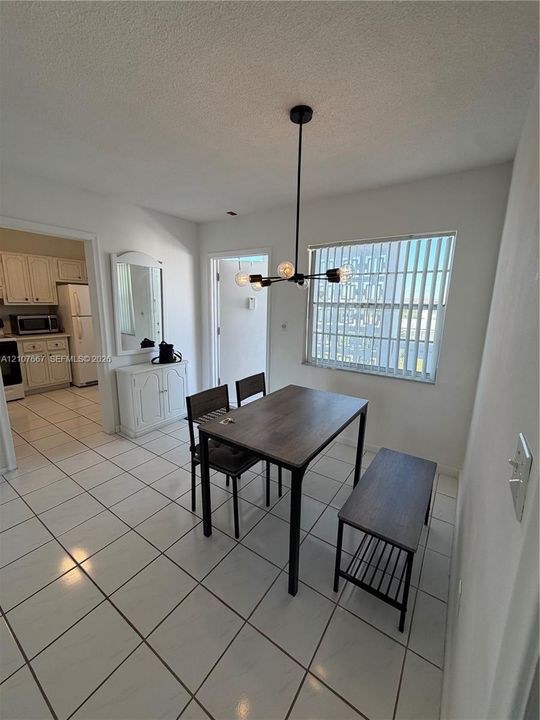 Dining area featuring white ceramic tile flooring, a modern multi-arm matte black chandelier, and a wall-mounted mirror
