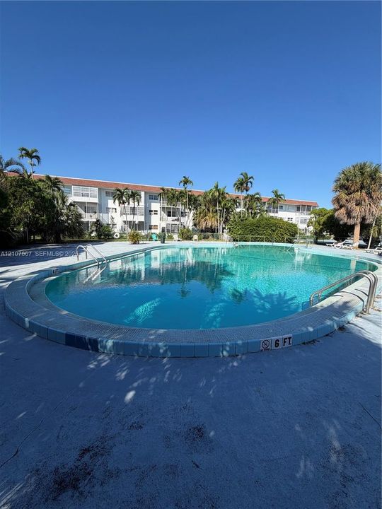 Sparkling resort-style pool with curved perimeter and sun deck, surrounded by mature tropical landscaping including palm trees and native vegetation