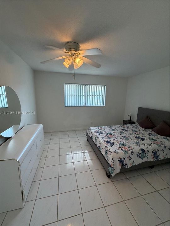 Neutral-toned interior featuring ceramic tile flooring, a central multi-blade ceiling fan with integrated light fixture, and horizontal blind window treatments