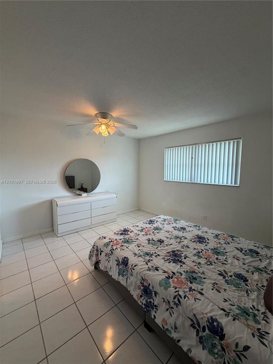 Neutral-toned room featuring tile flooring, a multi-blade ceiling fan with integrated lighting, and vertical window blinds