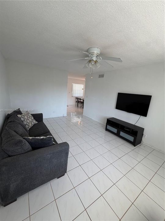 Neutral-toned ceramic tile flooring throughout, ceiling fan with integrated light fixture, and textured ceilings
