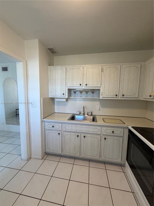 Kitchen featuring light-toned cabinetry, solid-surface countertops, an integrated stainless steel sink, and white ceramic tile flooring