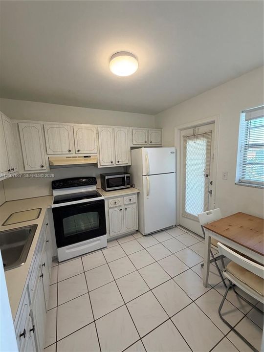 Kitchen featuring white cabinetry, solid-surface countertops, tile flooring, and an exterior door with integrated screen
