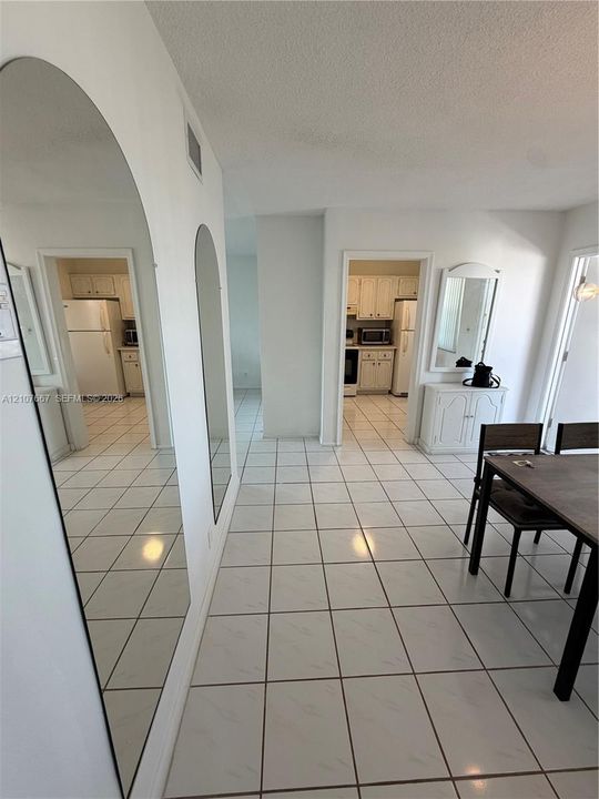 Large arched wall mirrors, white ceramic tile flooring, and built-in cabinetry featuring white shaker-style doors