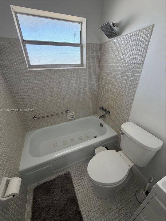 Bathroom featuring a square-tile surround, porcelain-finish soaking tub, ceiling-mounted rainfall showerhead, and a wall-mounted metal grab bar