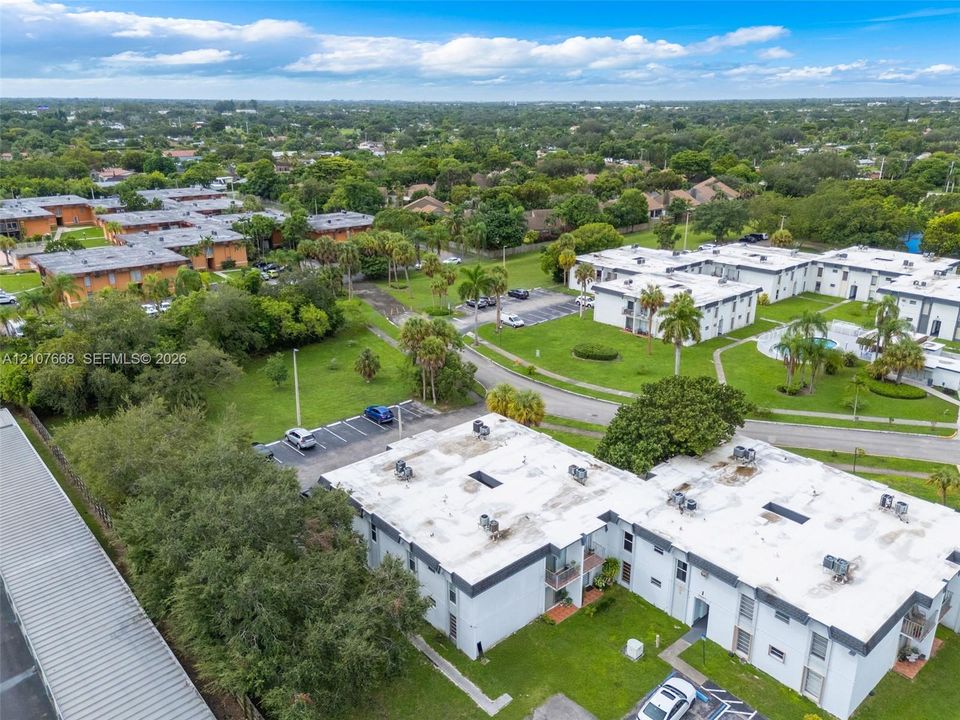 Aerial perspective featuring multi-unit structures, landscaped grounds with mature palm trees, dedicated surface parking, and a communal swimming pool