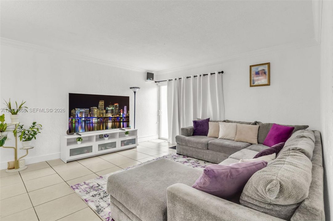 Living area featuring neutral tile flooring, crown molding, and a sliding glass door