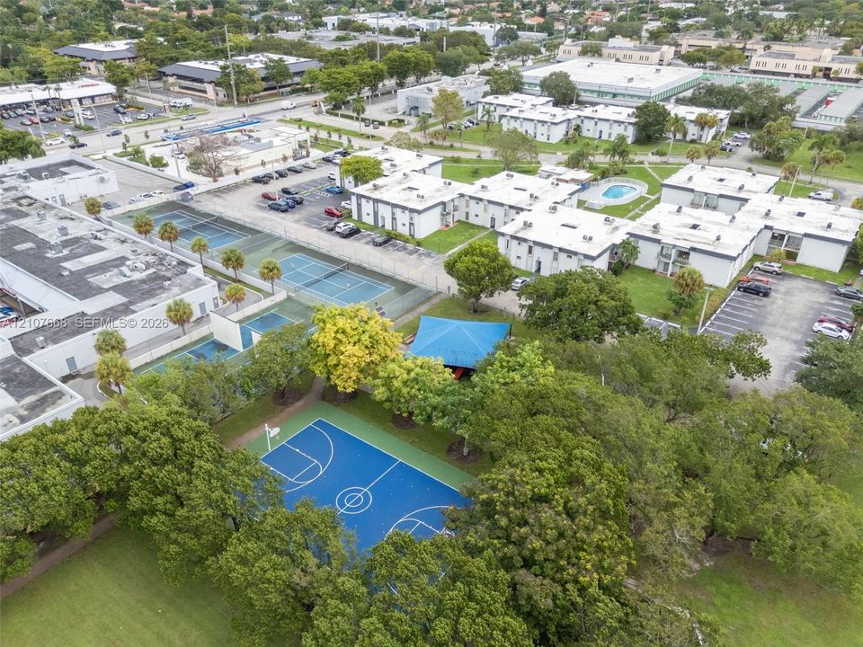 Aerial perspective featuring a basketball court, multiple tennis courts, an outdoor swimming pool, and a shaded pavilion