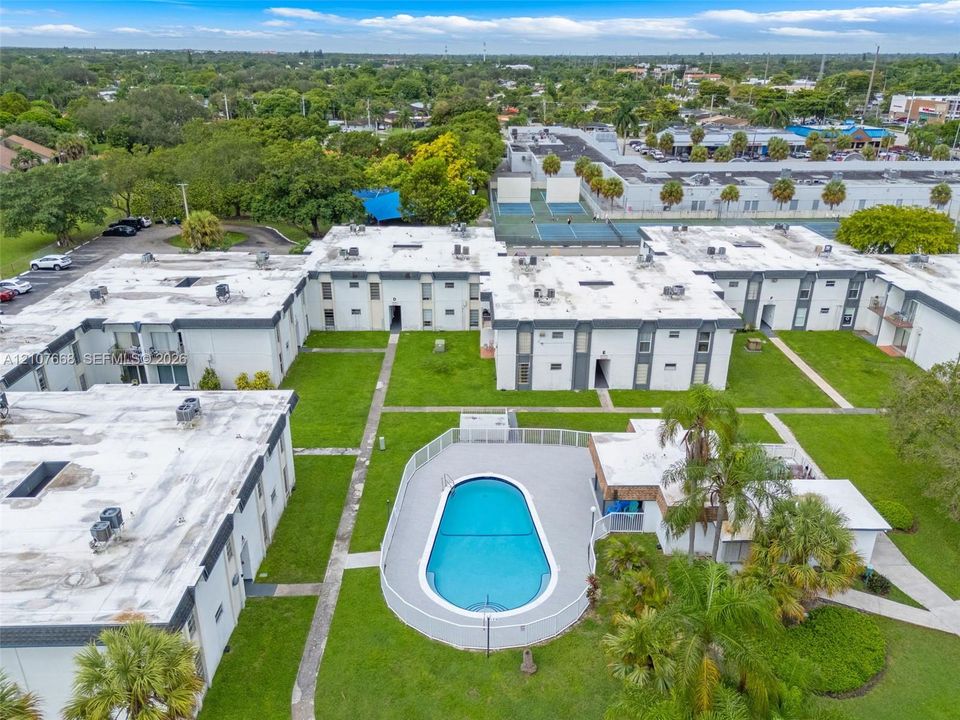 Aerial perspective of the multi-unit complex featuring an outdoor swimming pool with surround decking, mature palms, manicured lawns, and paved walkways