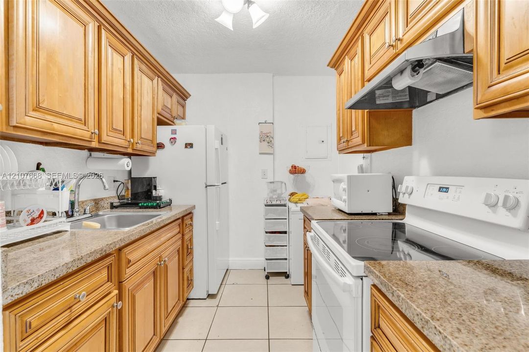 Kitchen featuring natural wood cabinetry, stone-finish countertops, ceramic tile flooring, and a stainless steel sink with an arch-neck faucet
