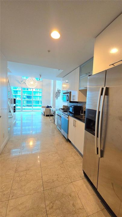 Kitchen featuring high-gloss cabinetry, stainless steel appliances, and stone tile flooring