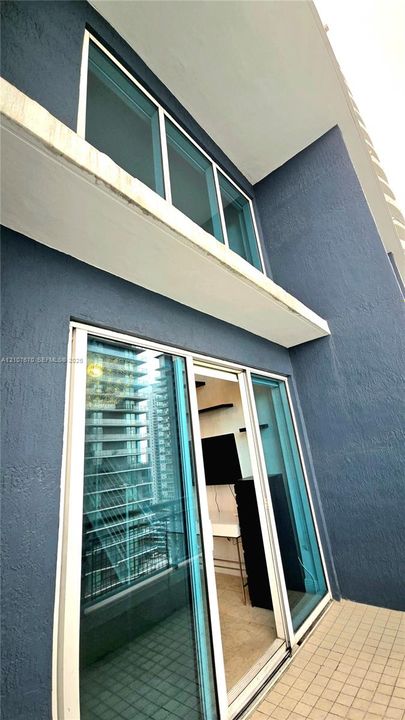 Textured blue stucco exterior featuring floor-to-ceiling glass sliding doors, a white structural overhang, and square ceramic tile flooring