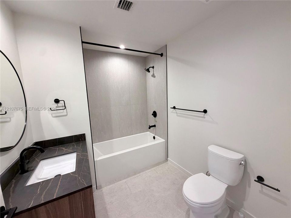 Bathroom featuring a vanity with dark stone-patterned countertop, integrated sink, wood-finish cabinetry, matte black plumbing fixtures, and a tub-shower combination with floor-to-ceiling tile surround