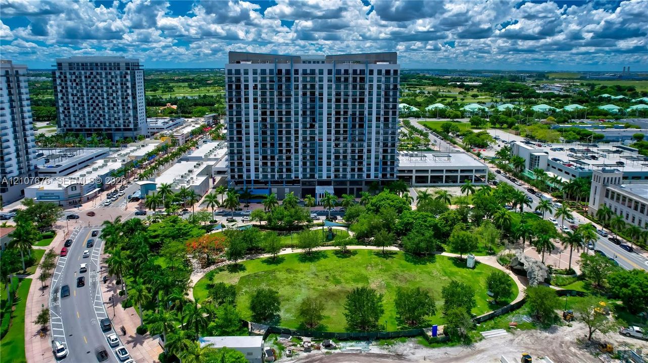 High-rise residential building featuring a glass and concrete facade, integrated parking structure, and extensive green space with established landscaping