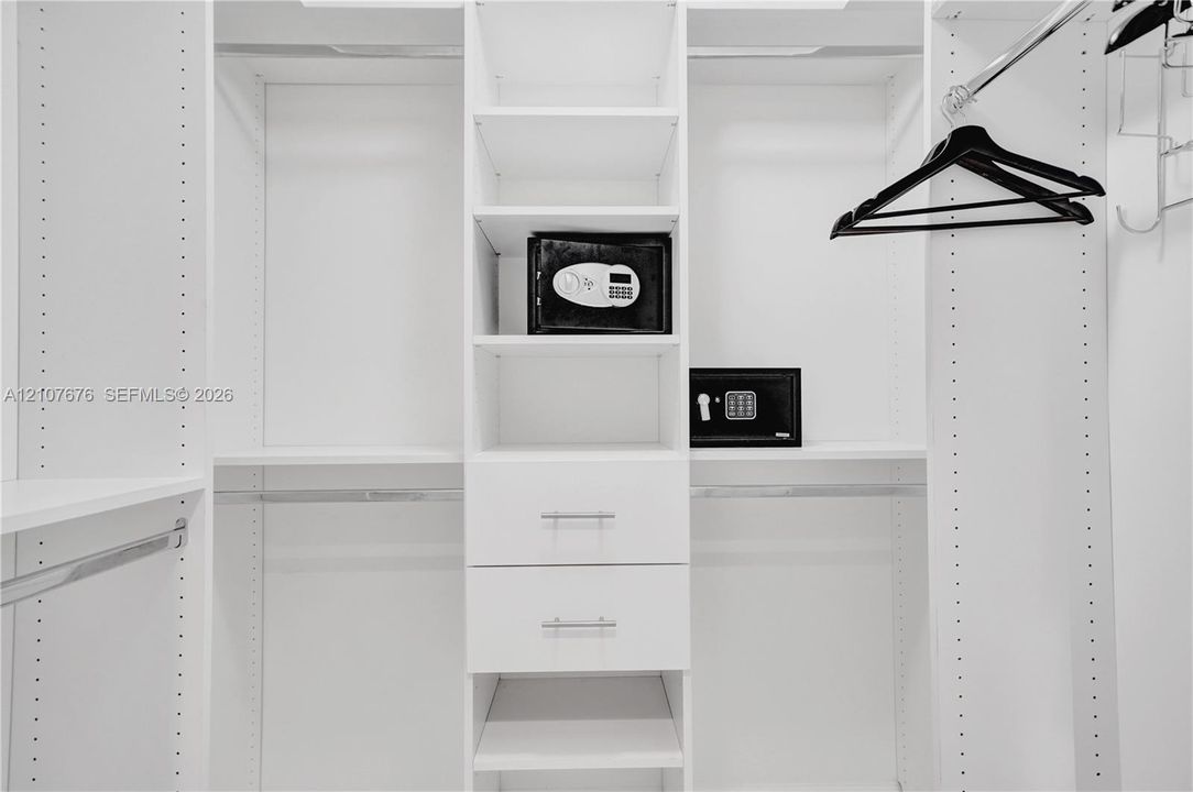 Custom walk-in closet featuring white laminate built-in cabinetry, adjustable shelving, dual soft-close drawers with silver-tone pulls, and integrated garment rods