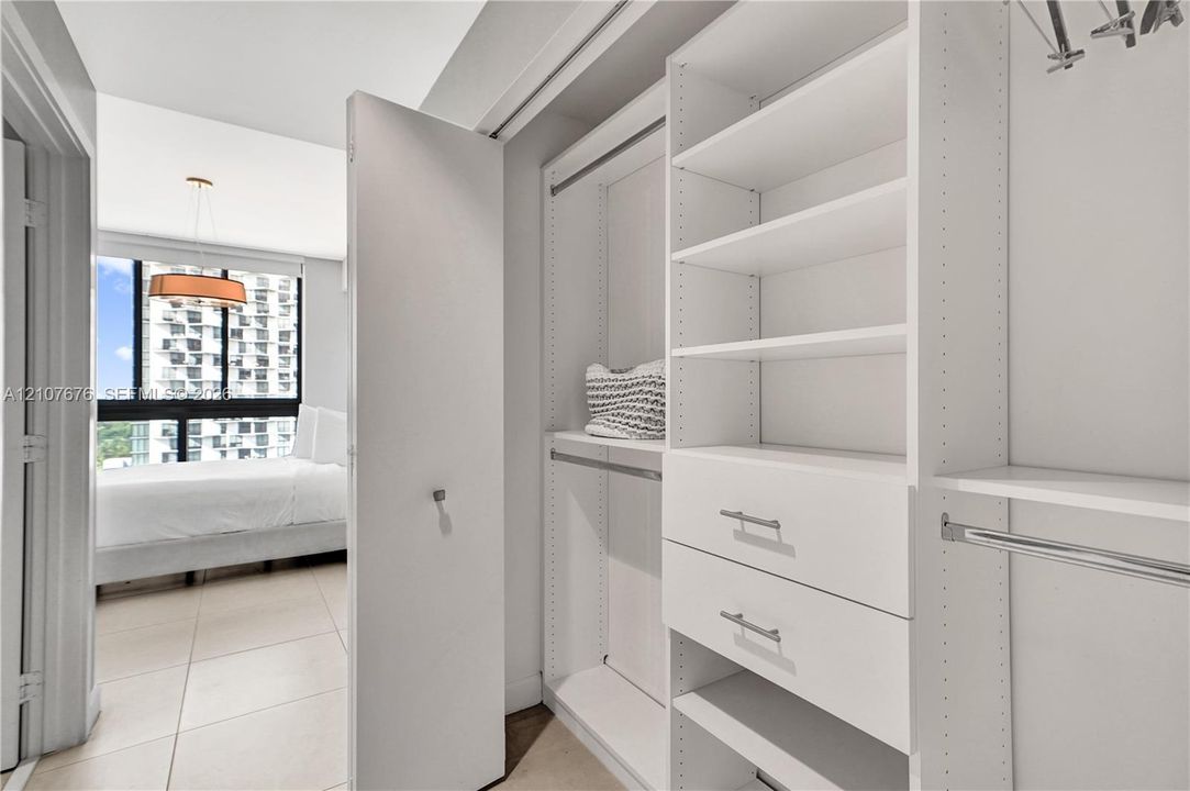 Custom reach-in closet featuring white built-in shelving, dual soft-close drawers, metal garment rods, and integrated cabinetry hardware