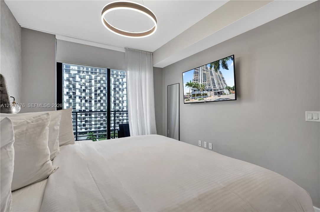 Floor-to-ceiling glass sliding doors opening to a private balcony, contemporary circular LED chandelier, and wall-mounted television