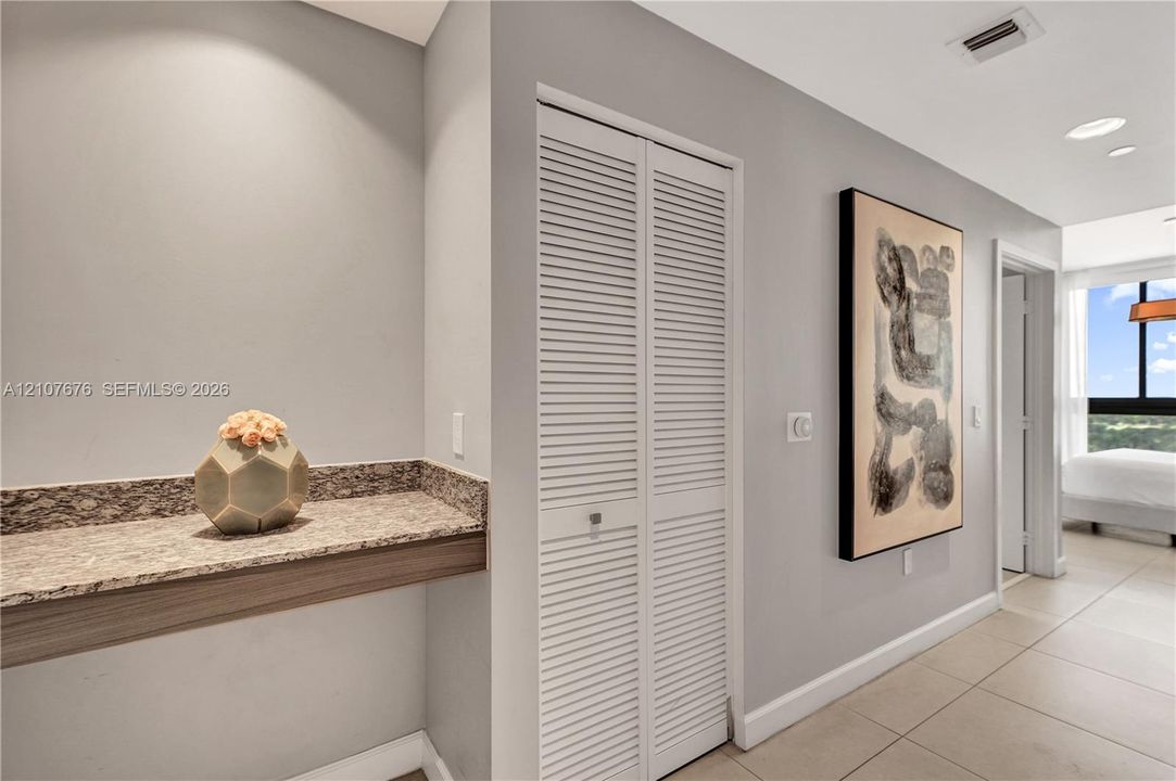 Built-in stone-surface desk with wood-finish trim, bi-fold louvered closet doors, and large-format tile flooring