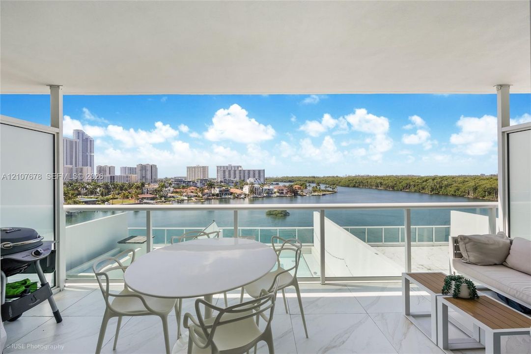 Covered balcony featuring large-format stone tile flooring and a glass-paneled railing overlooking the water