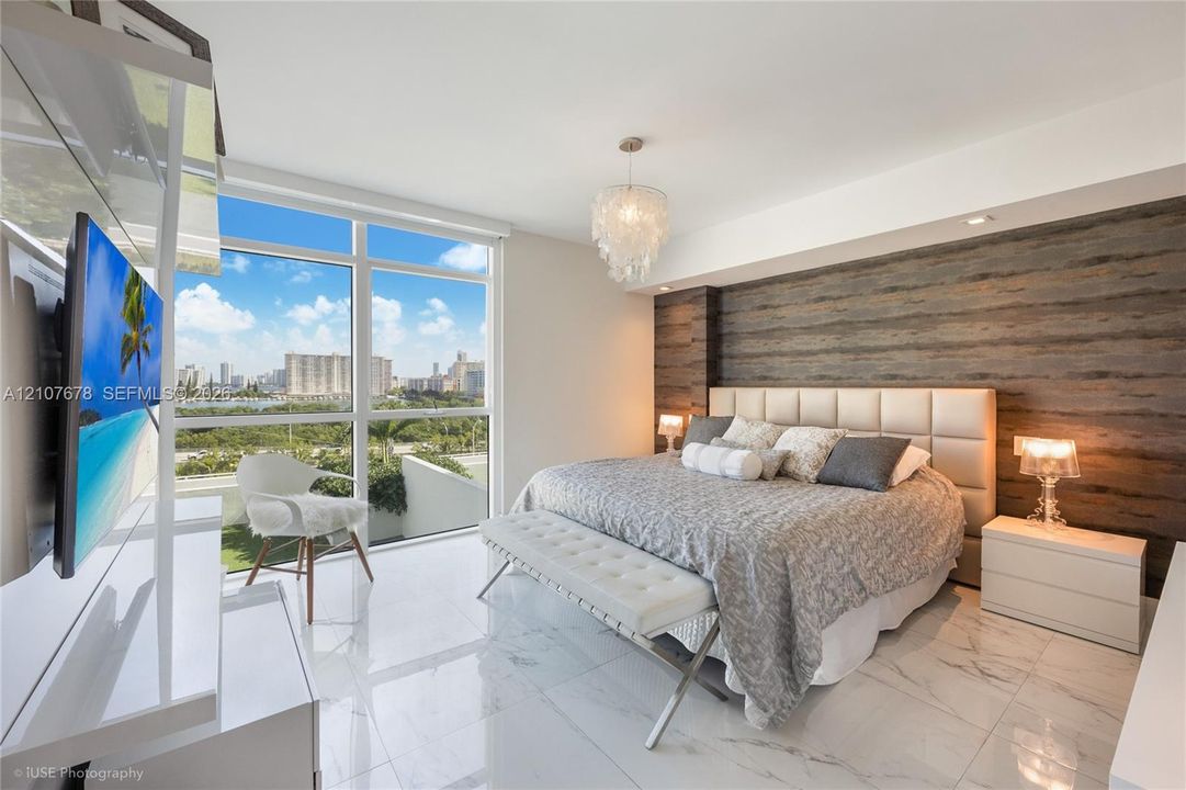 Floor-to-ceiling windows, wood-panel accent wall, polished stone-finish flooring, and decorative chandelier