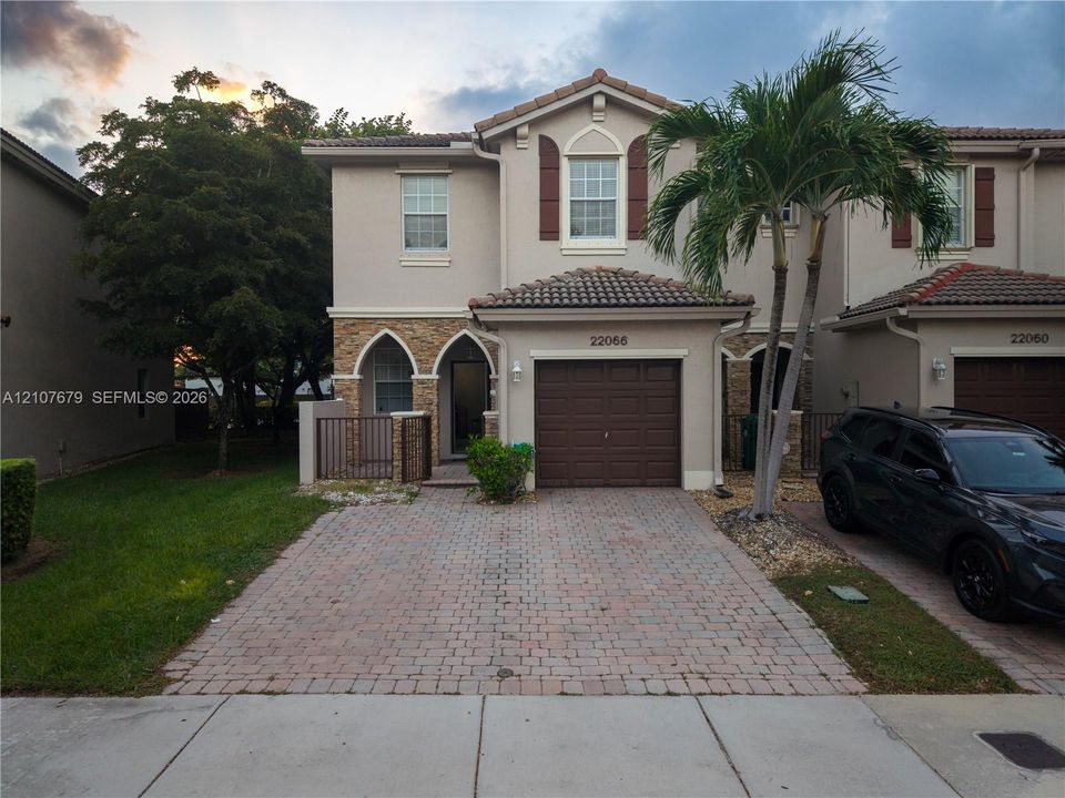 Two-story residence featuring a tile roof, stucco exterior with stone veneer accents, arched entryway, brick-paver driveway, and an attached single-car garage