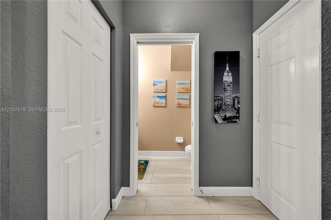Interior hallway featuring neutral grey wall paint, two white six-panel closet doors, a white interior door, and ceramic tile flooring