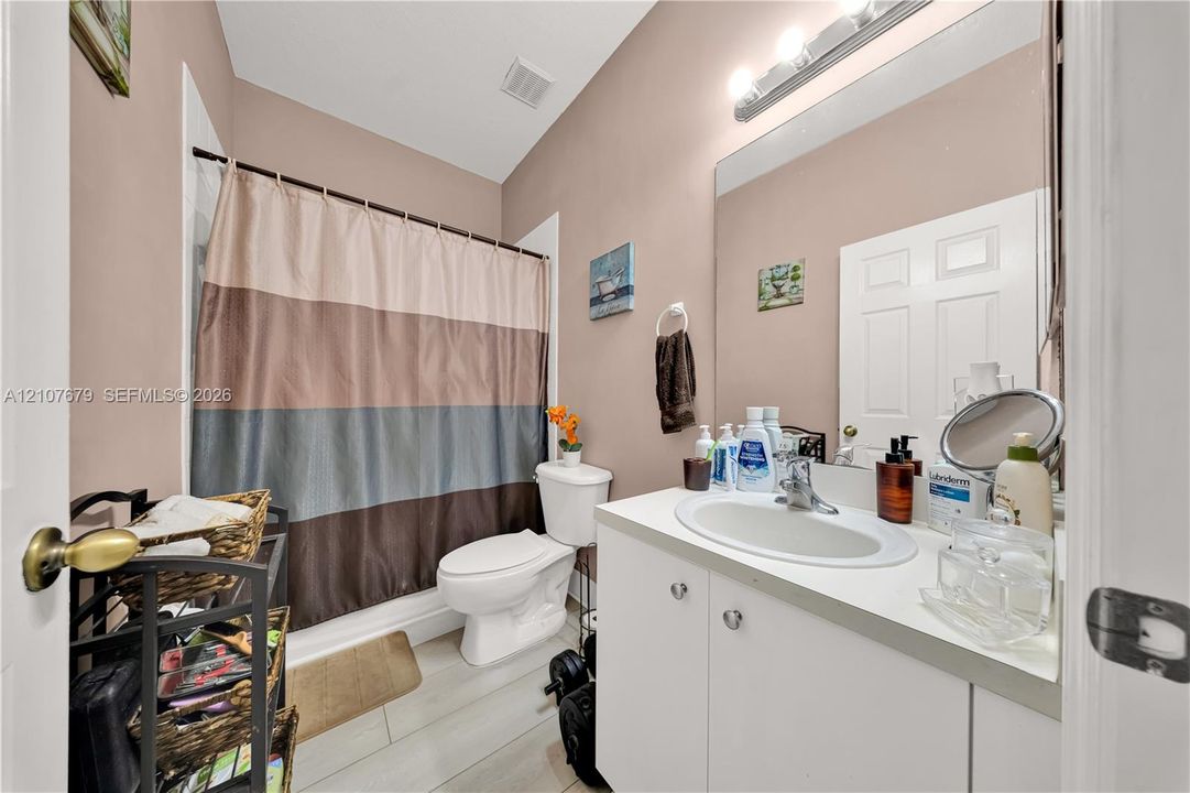 Bathroom featuring a white vanity cabinet with an integrated oval sink, a large wall-mounted mirror, a tub-shower combination, and wood-finish flooring