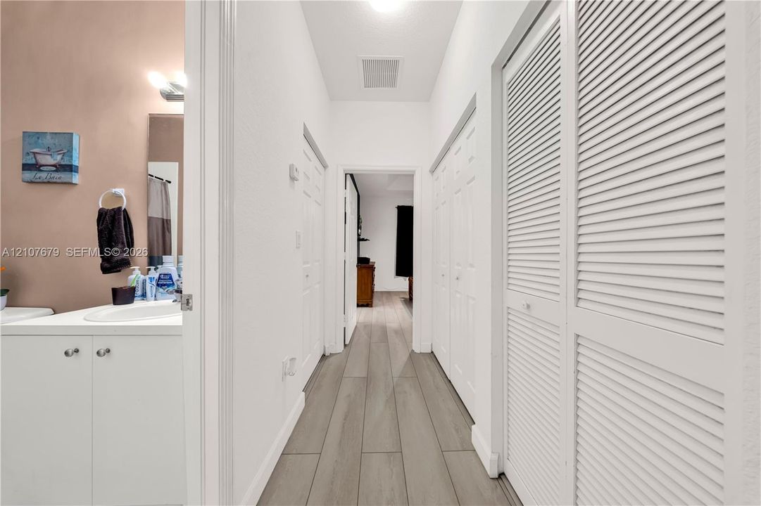 Wood-finish flooring, white cabinetry with integrated sink, and dual white louvered-style closet doors