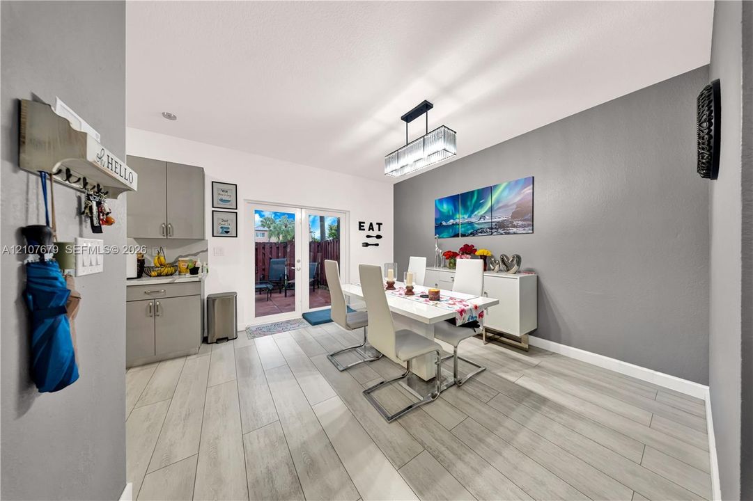 Dining area featuring wood-finish tile flooring, grey cabinetry with solid-surface countertops, dual glass-paned doors, and a rectangular multi-light pendant fixture