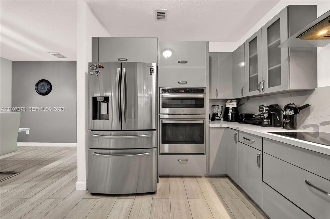 Kitchen featuring flat-panel gray cabinetry, stainless steel built-in double ovens, stainless steel French door refrigerator, solid surface countertops, and wood-finish flooring