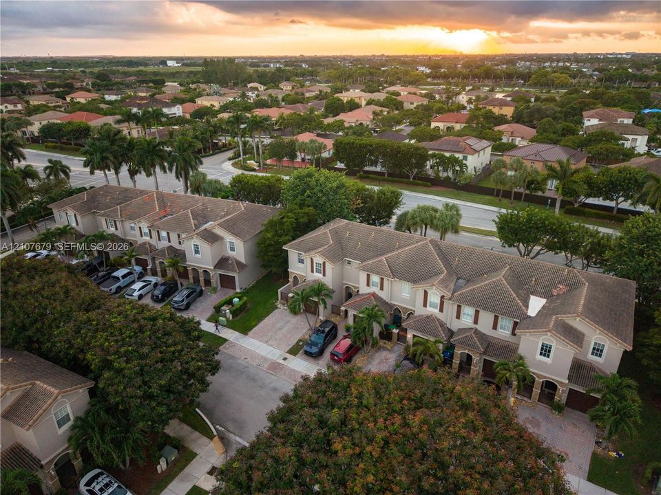 Aerial perspective of a multi-unit residential community featuring paver driveways, pitched shingle roofing, and established landscaping