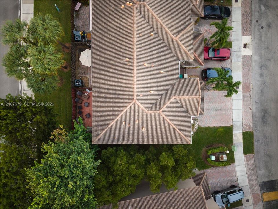 Aerial perspective featuring a multi-hipped tile roof, paver driveway, and mature landscaping