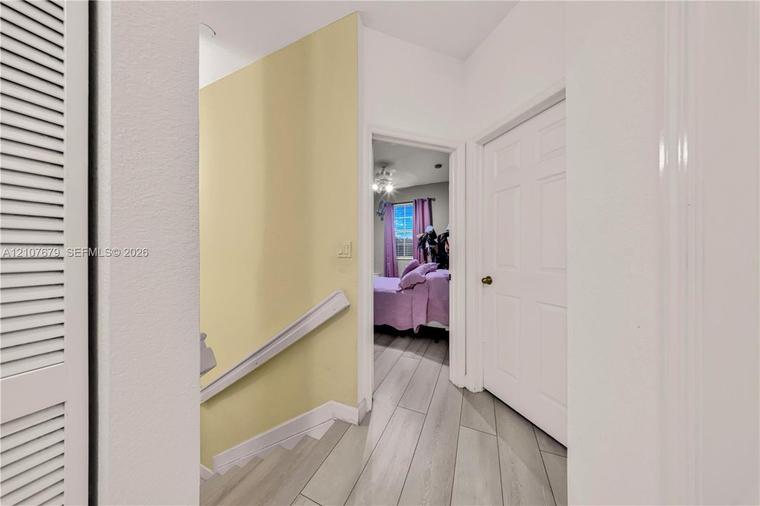 Hallway featuring wood-finish tile flooring, white paneled interior doors, and a louvered closet door