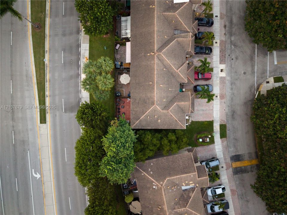 Aerial view of multi-unit residential complex featuring shingle roofing, paved parking areas, and mature landscaping
