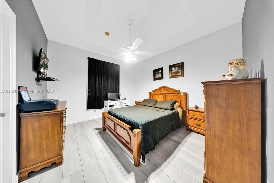 Room featuring tray ceiling, wood-finish flooring, and a ceiling fan with integrated lighting