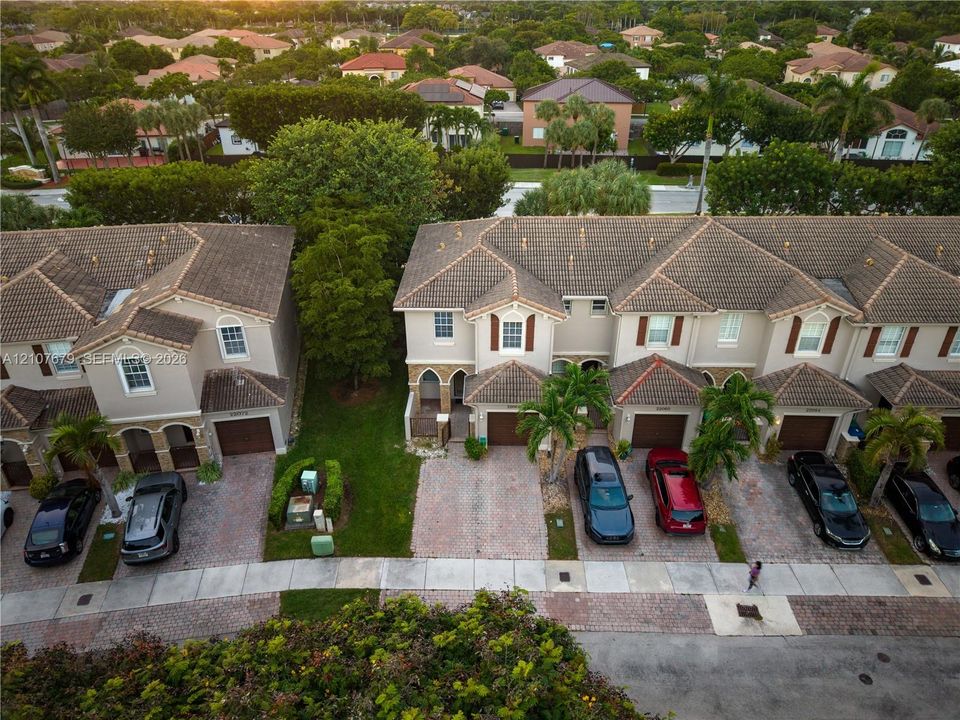 Aerial perspective of multi-family residences featuring clay tile roofing, paved driveways, arched architectural detailing, and integrated garage spaces