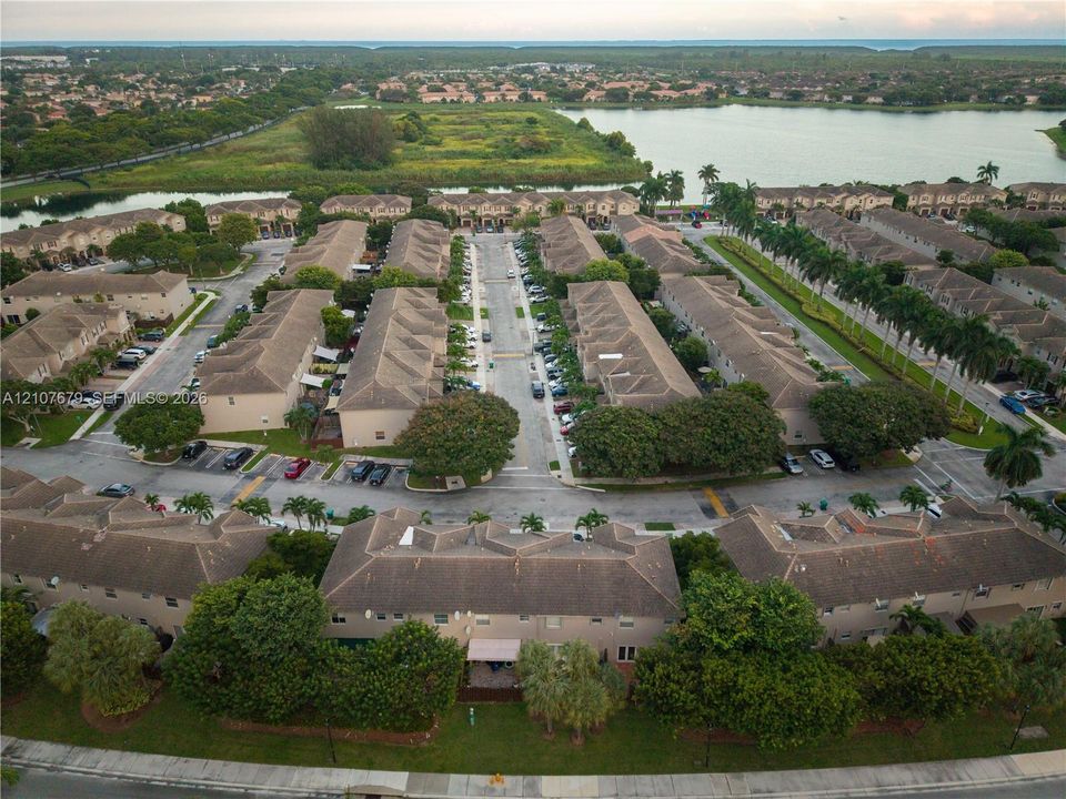 Aerial perspective featuring a multi-building residential complex with pitched roofs, paved streets, and expansive green space bordering a large lake