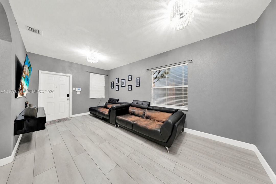 Interior space featuring wood-finish flooring, neutral gray wall paint, dual crystal-style chandeliers, and a white paneled entry door