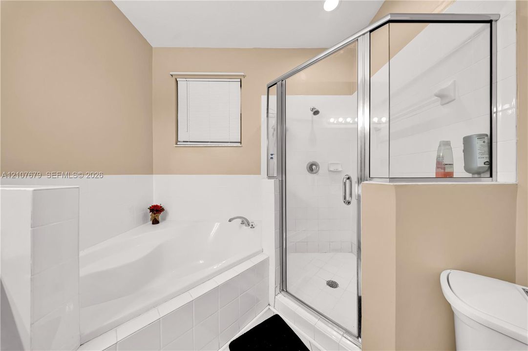 Corner soaking tub with tile surround, glass-enclosed shower, and polished chrome fixtures