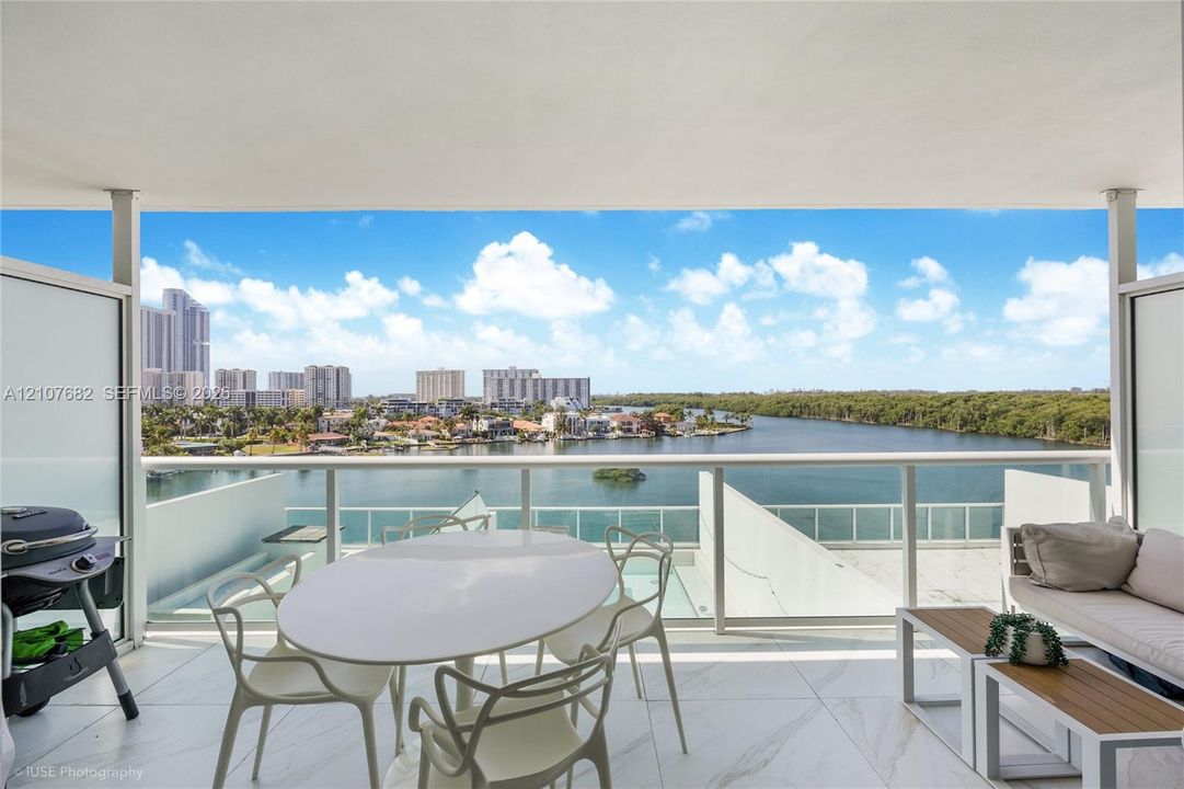 Covered balcony featuring large-format stone tile flooring and a glass-paneled railing overlooking the water