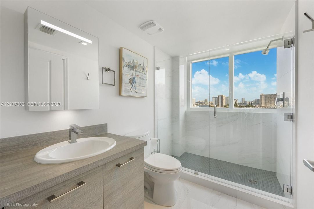 Bathroom featuring a wood-finish vanity with an integrated oval sink, glass-enclosed shower with tiled surround, and large-scale window