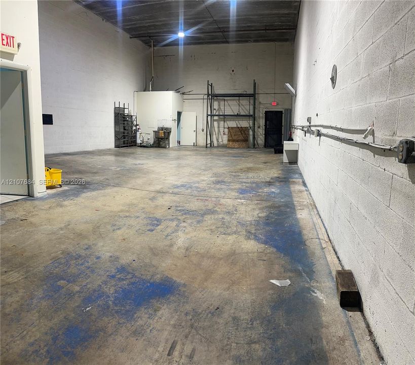 Industrial space featuring exposed concrete block walls, high ceilings, concrete flooring, and metal racking units