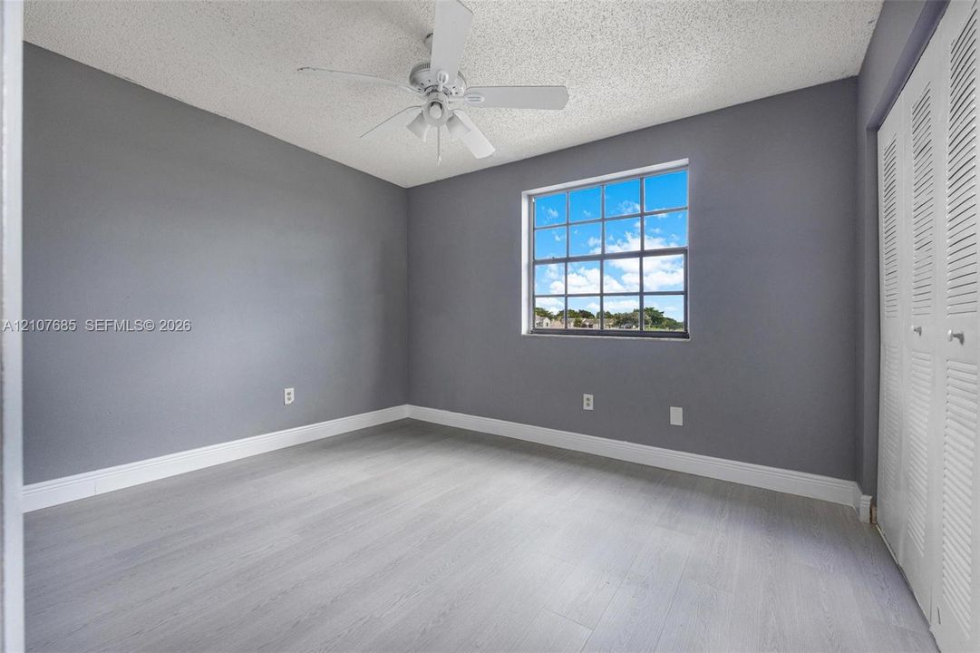Room featuring gray walls, wood-finish flooring, a multi-pane window, a ceiling fan, and louvered bifold closet doors